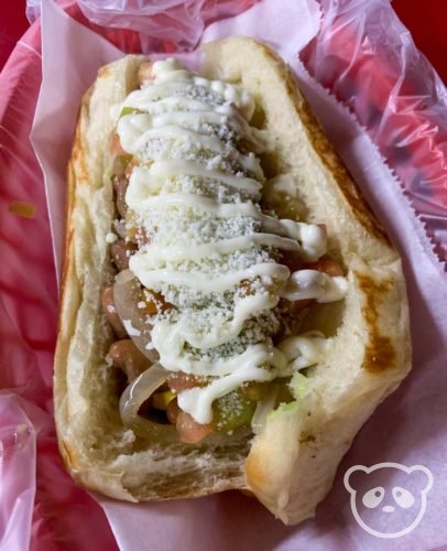 Sonoran hot dog wrapped with bacon, cheese, mayonnaise, pinto beans, and avocado.