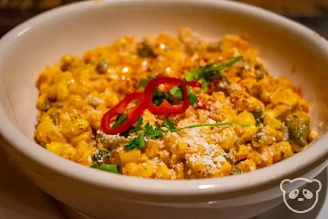 Bowl of elote corn topped with cheese and chili pepper slices. 