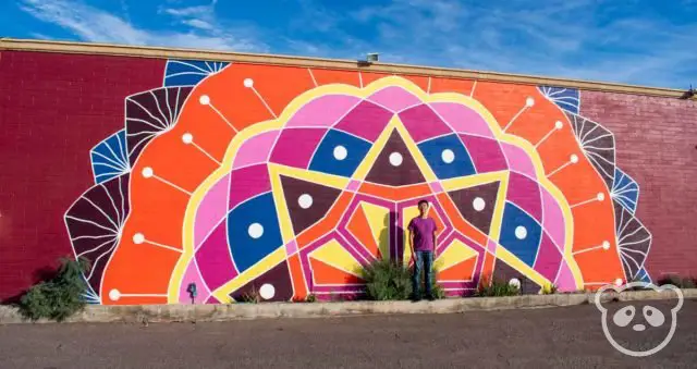 Colorful mandala mural located on the side of a building with Jimmy in front of it. 