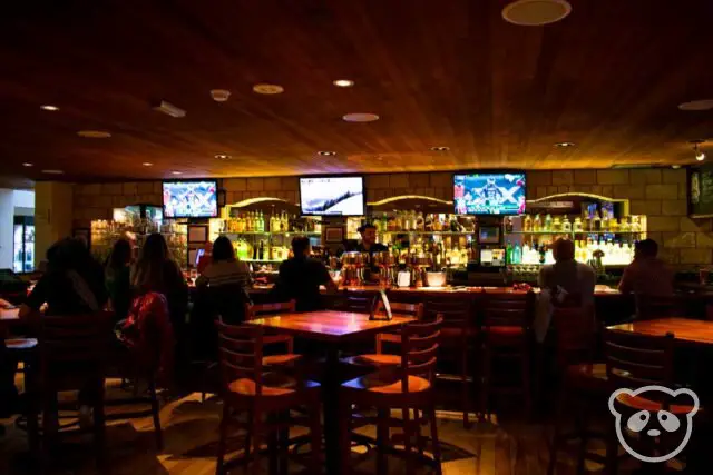 Interior of sports bar with bar, bartender, tables, and customers. 