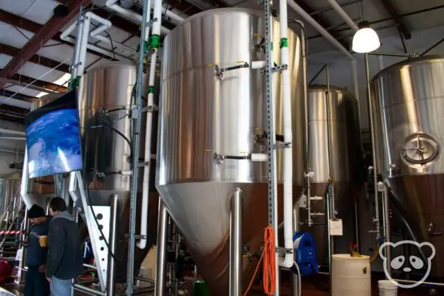 Two men standing next to the fermenters at the brewery.