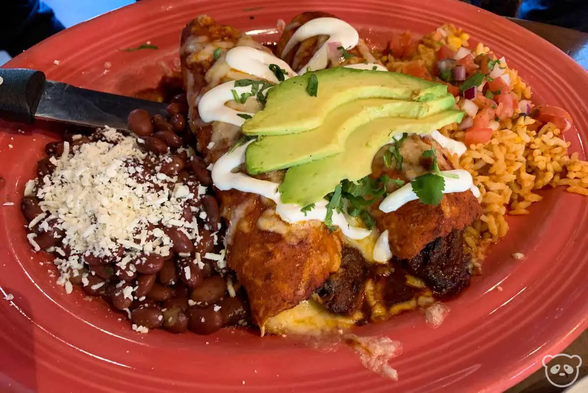 Beef enchiladas, beans, and rice on a plate. 