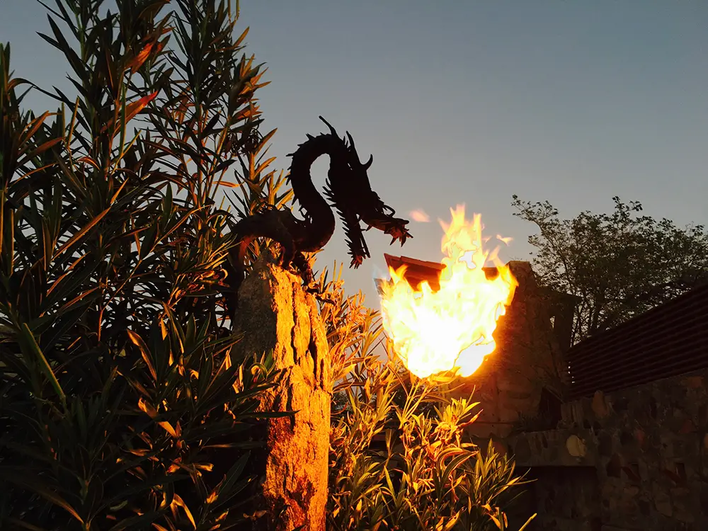 Metal dragon breathing fire from above a wall.