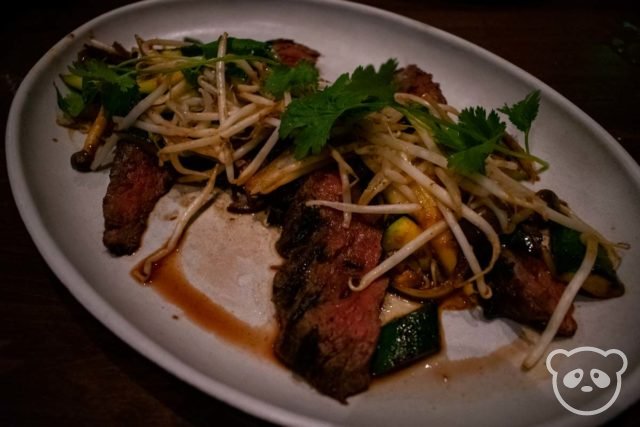 Plate of steak with bean sprouts and cilantro.