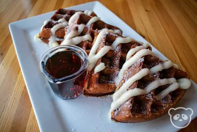 Gingerbread waffles with white icing, peppermint shavings on top, and a side of maple syrup. 