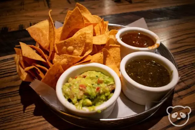 Tortilla chips with dips including guacamole, and 2 different salsas.