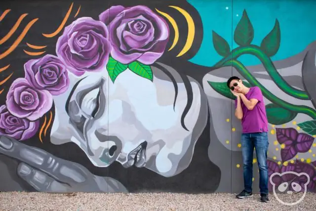 Jimmy posing next to the mural of a sleeping woman with flowers in her hair. 
