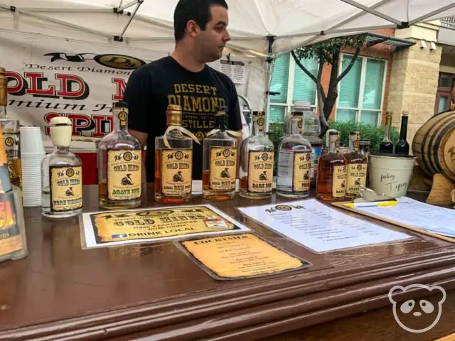 Man behind the stall with a table top full of whiskey, rum, and vodka bottles.