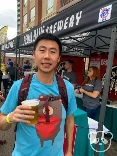 A man holding a beer with the festival stall behind him.