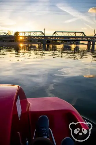 Photo of feet pedaling on the pedal boat with Tempe Town Lake and Tempe Town Lake Pedestrian Bridge around sunset. 