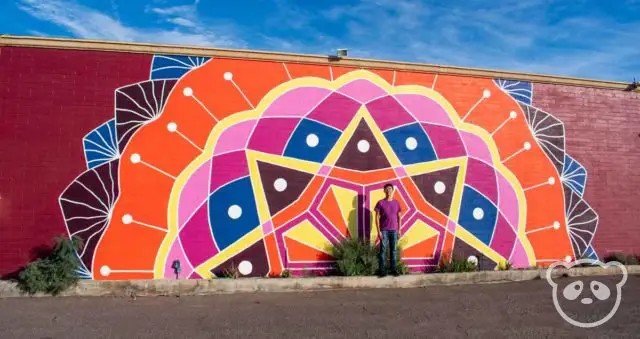 Colorful mandala mural located on the side of a building with Jimmy in front of it.