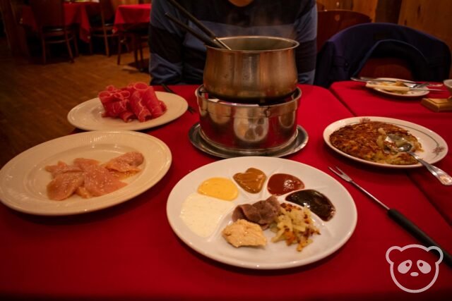 Table with plates of food for dipping into the pot of broth for fondue,