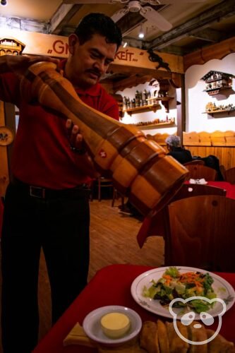 Restaurant server with pepper grinder seasoning salad. 