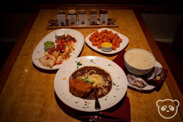 Tabletop of beer flight, 2 plates of food, and 2 bowls of soup.