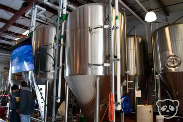 Two men standing next to the fermenters at the brewery. 