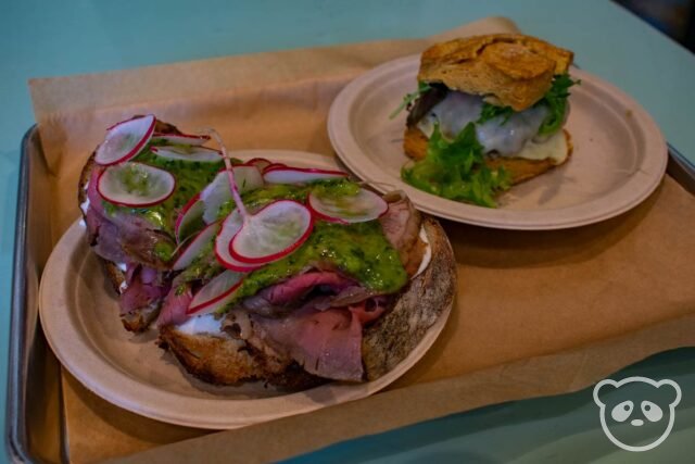 Metal tray with open faced beef sandwich on a plate next to a sausage biscuit sandwich on a plate.