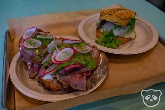 Metal tray with open faced beef sandwich on a plate next to a sausage biscuit sandwich on a plate. 