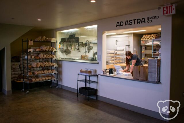 Bakery ordering window with loaves of bread and the kitchen shown. 