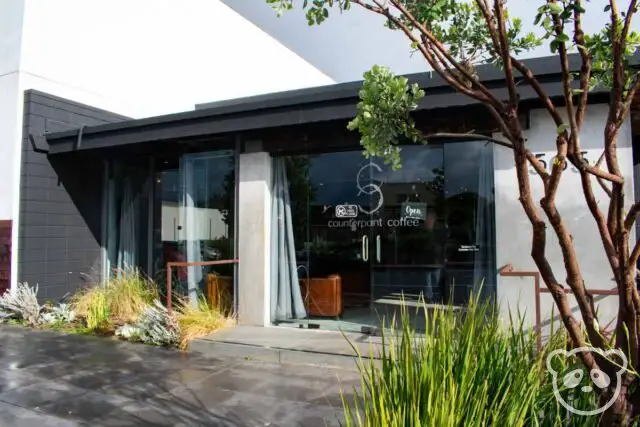 Cafe storefront with trees and grass planted in the front. 