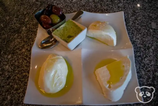 Plate of three different mozzarella cheeses with a pesto sauce and a dish of olives.