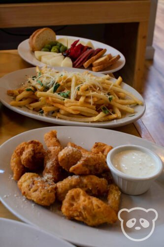Fried artichoke with aioli, garlic parmesan fries, and a charcuterie plate in the background.