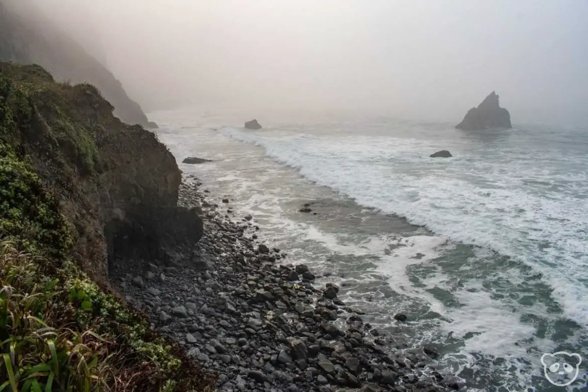 Cliffs and rocks to the left of the beach and sea stacks to the right in the ocean. 